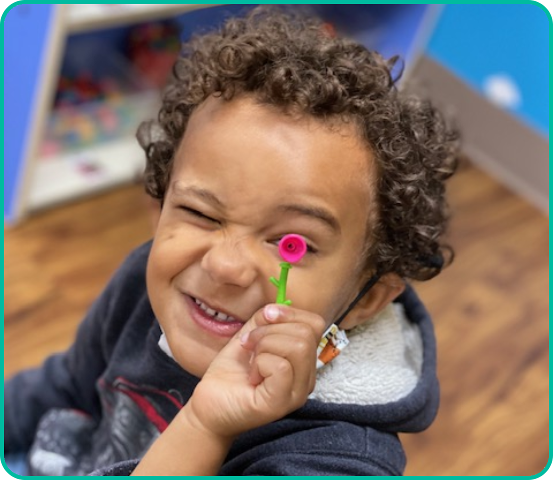 A young child holding a flower in front of his face.