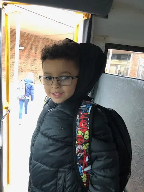 A boy with glasses and a backpack on the bus.